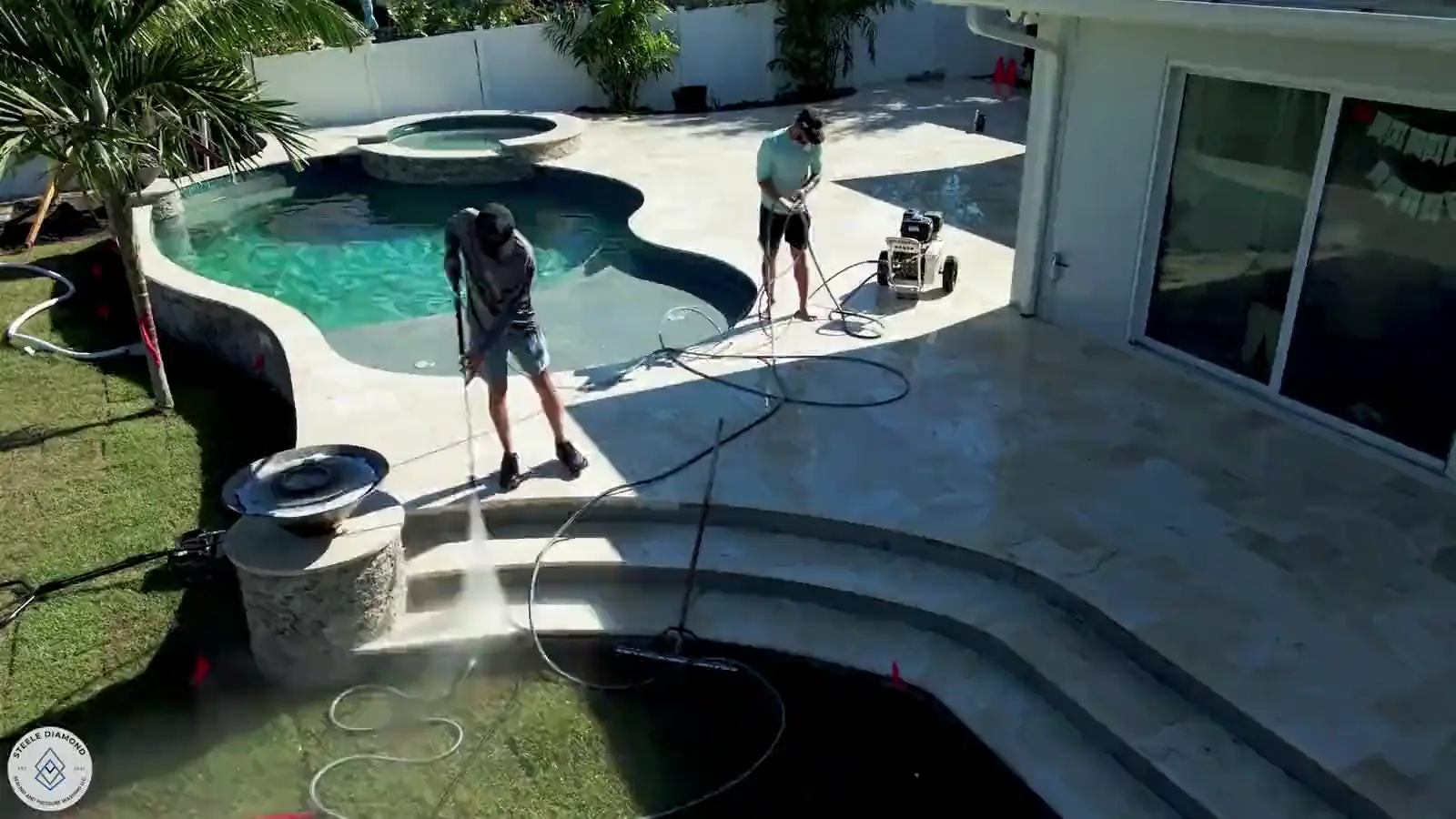 From the air: the Steele Diamond crew pressure washing a travertine pool deck beside a pool and spa.