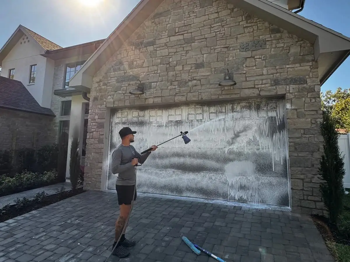 One of the crew soft washing a garage door on a stone house, the foam running down it.