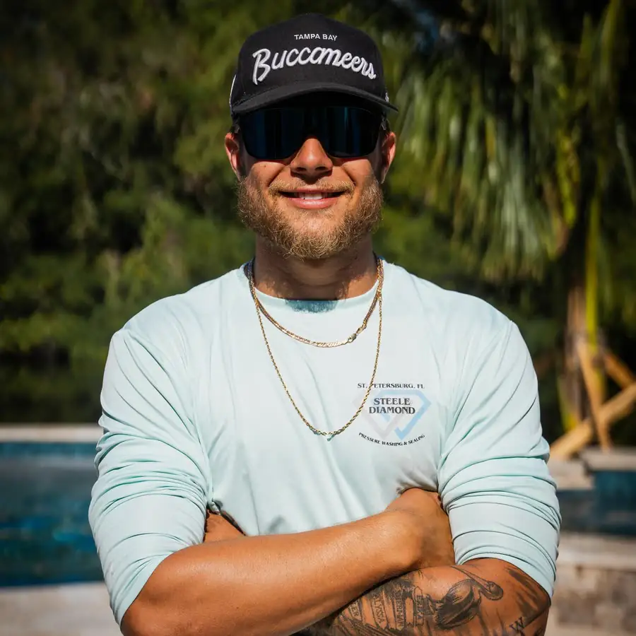 Cody Willoughby in a Steele Diamond shirt, Tampa Bay Buccaneers cap and sunglasses, arms crossed by a pool.