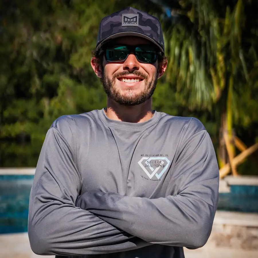 Gavrel Mead in a Steele Diamond shirt, cap and sunglasses, arms crossed and smiling by a pool.