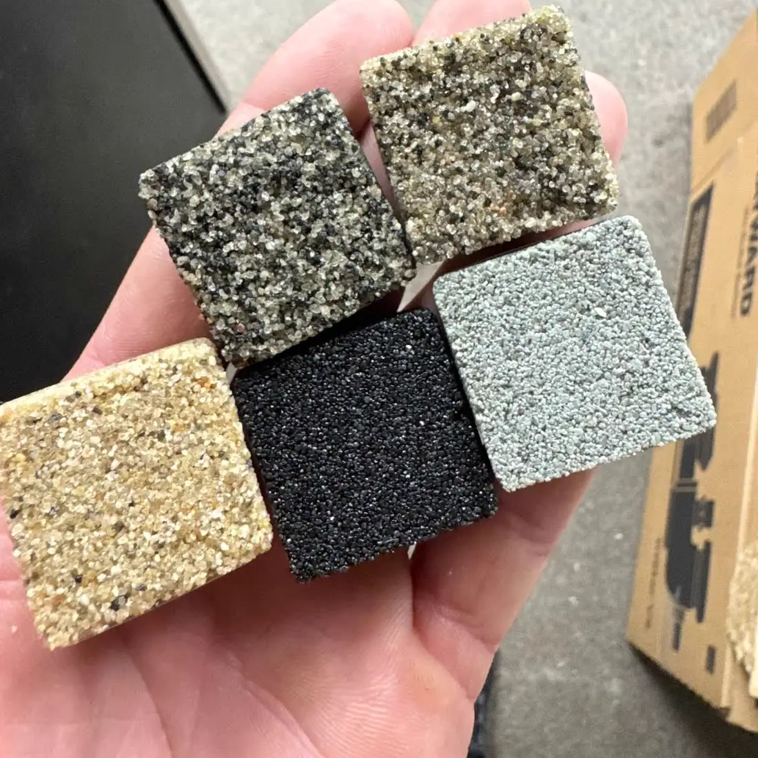 A hand holding four color samples of permeable joint sand.