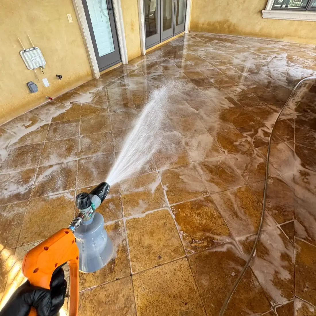 Pressure washing a stone patio under a covered lanai, the wet tile shining.