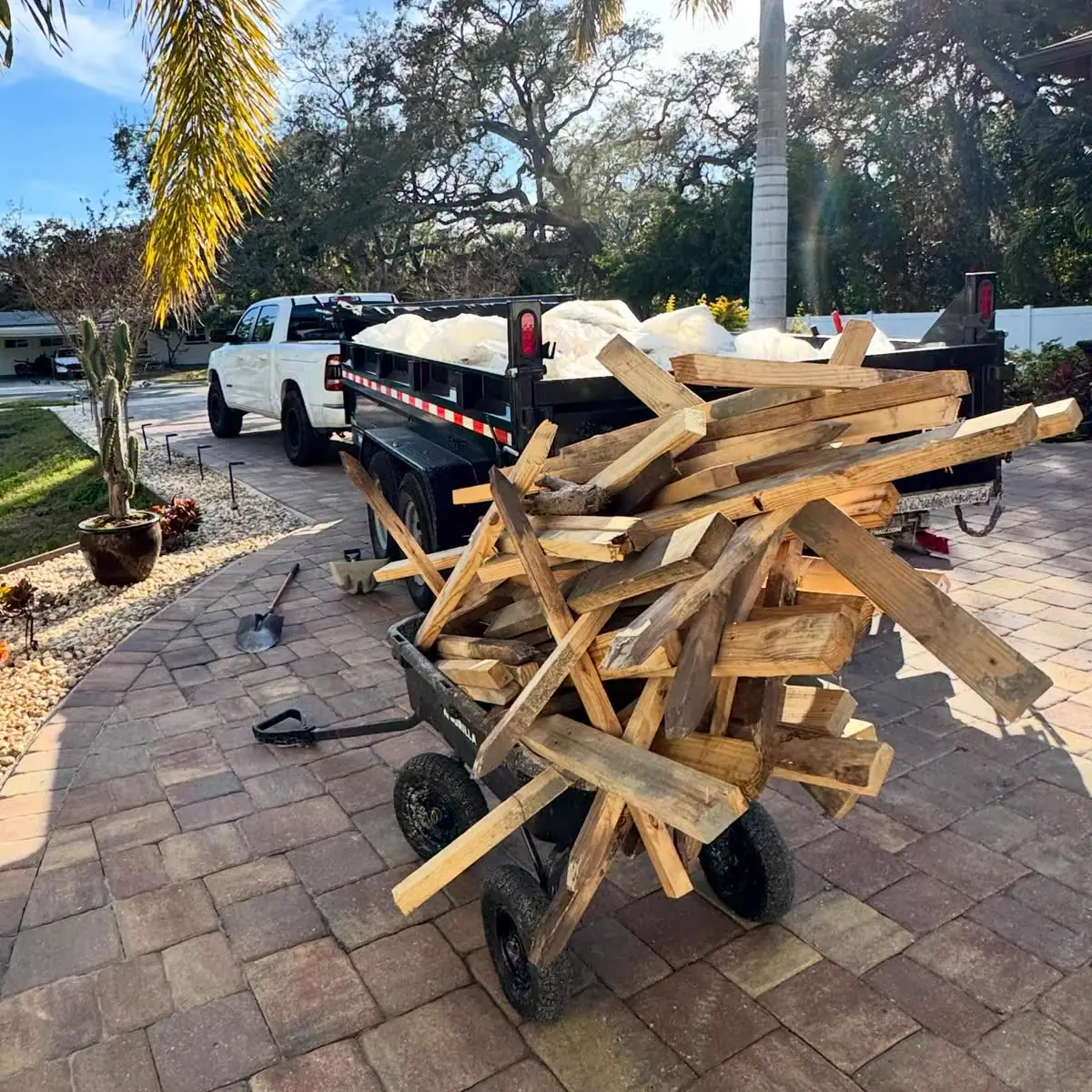 A dump trailer and a cart loaded with old lumber on a paver driveway.