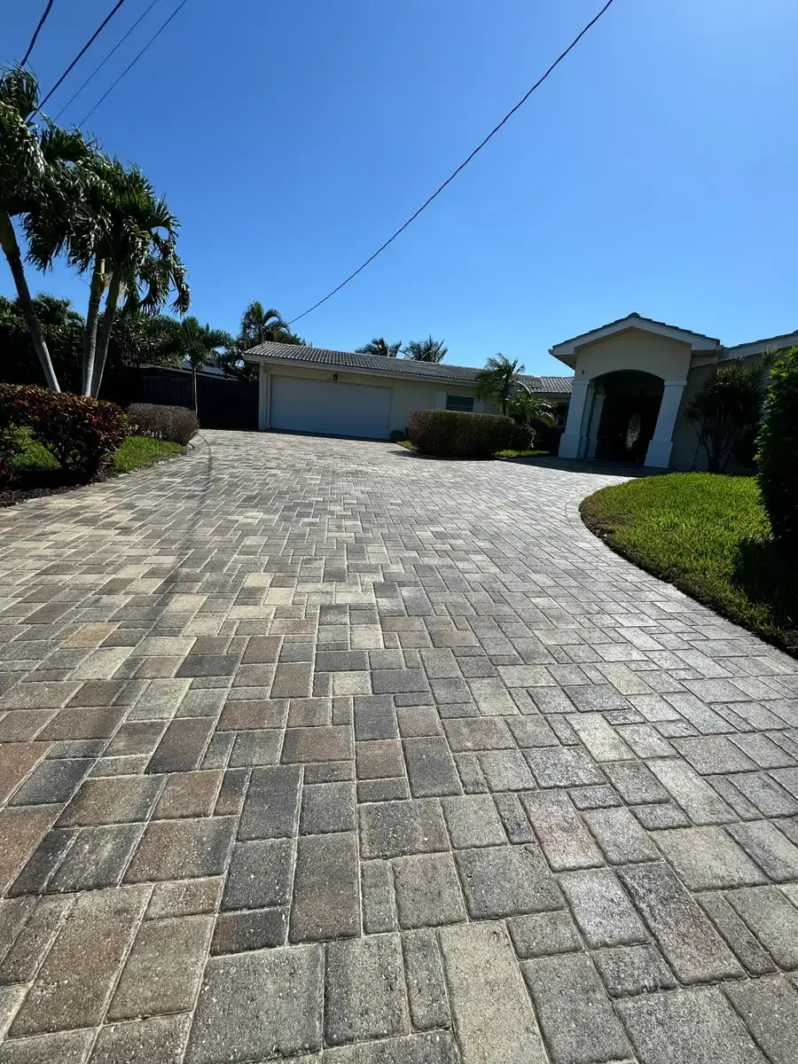 A long grey paver driveway leading to a house under palms.