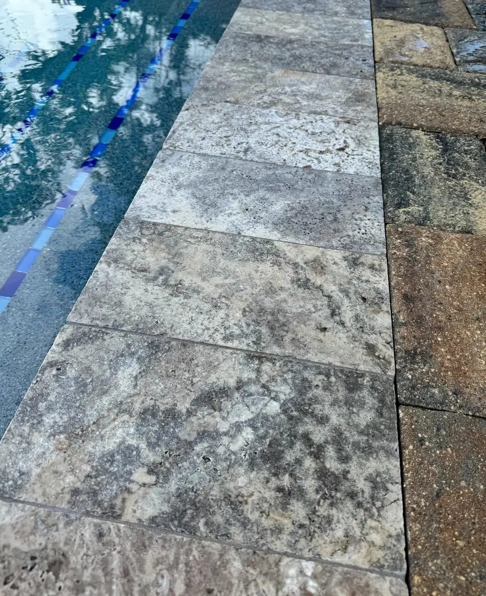 Travertine coping and pavers at the edge of a pool, close up.
