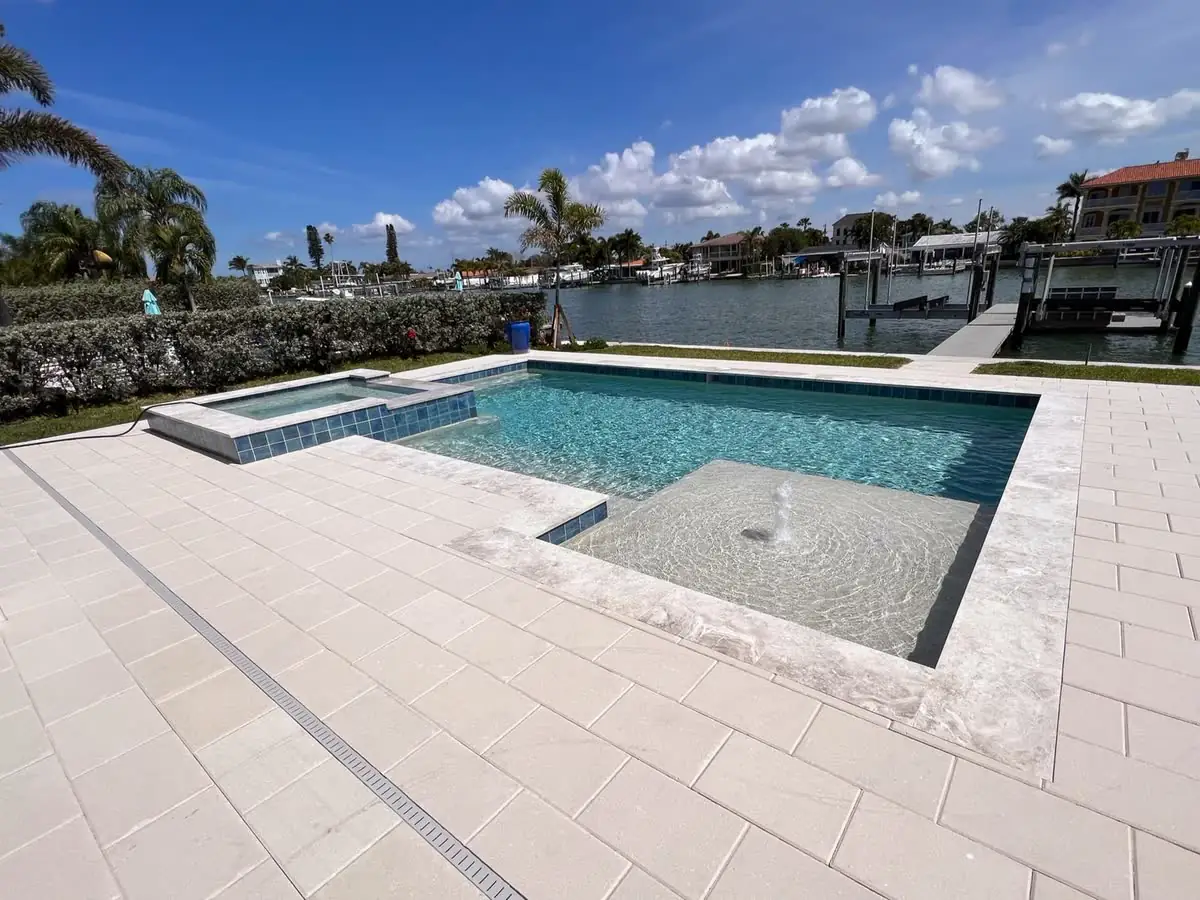 A white travertine pool deck and spa on a canal.