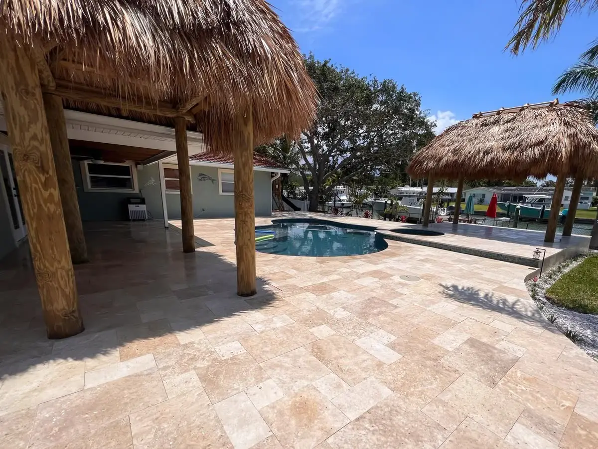 A travertine pool deck under thatched tiki huts.