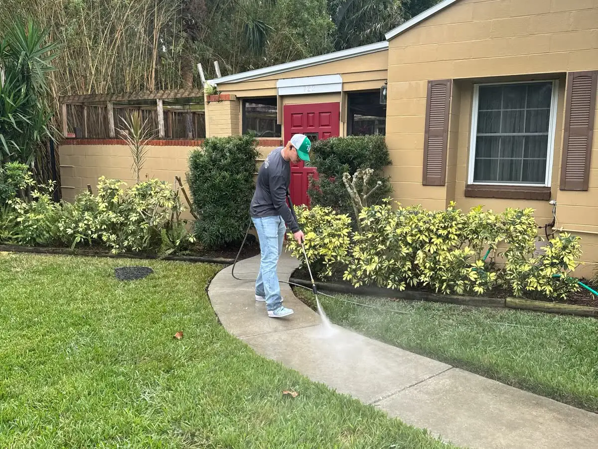 One of the crew washing a front walkway with a wand.