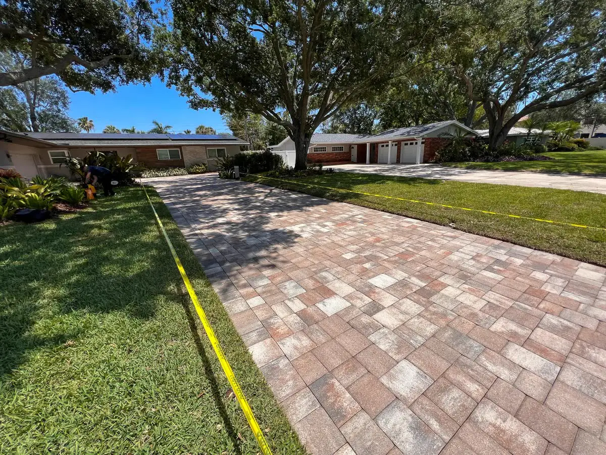 A brick paver walkway beside a lawn under big oaks.