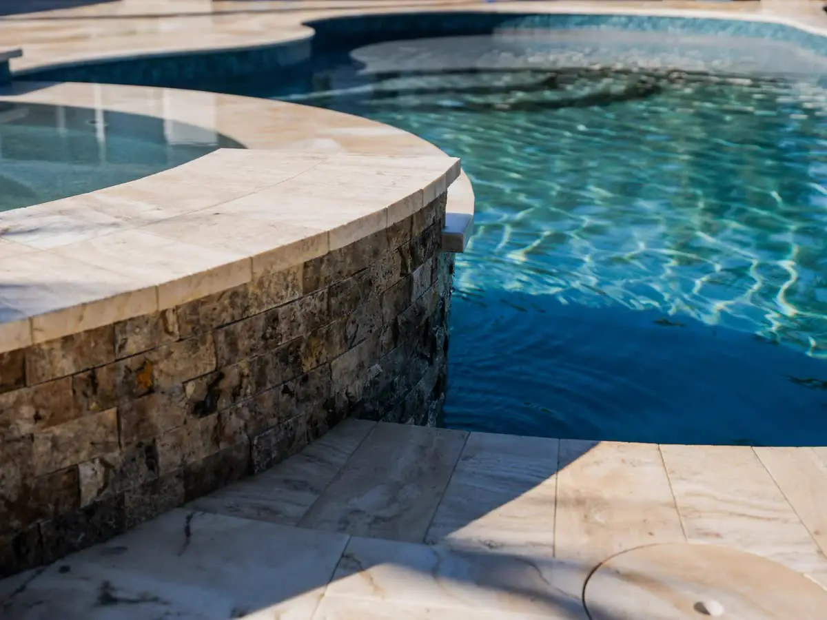 A pool edge with a stacked-stone wall and travertine coping.