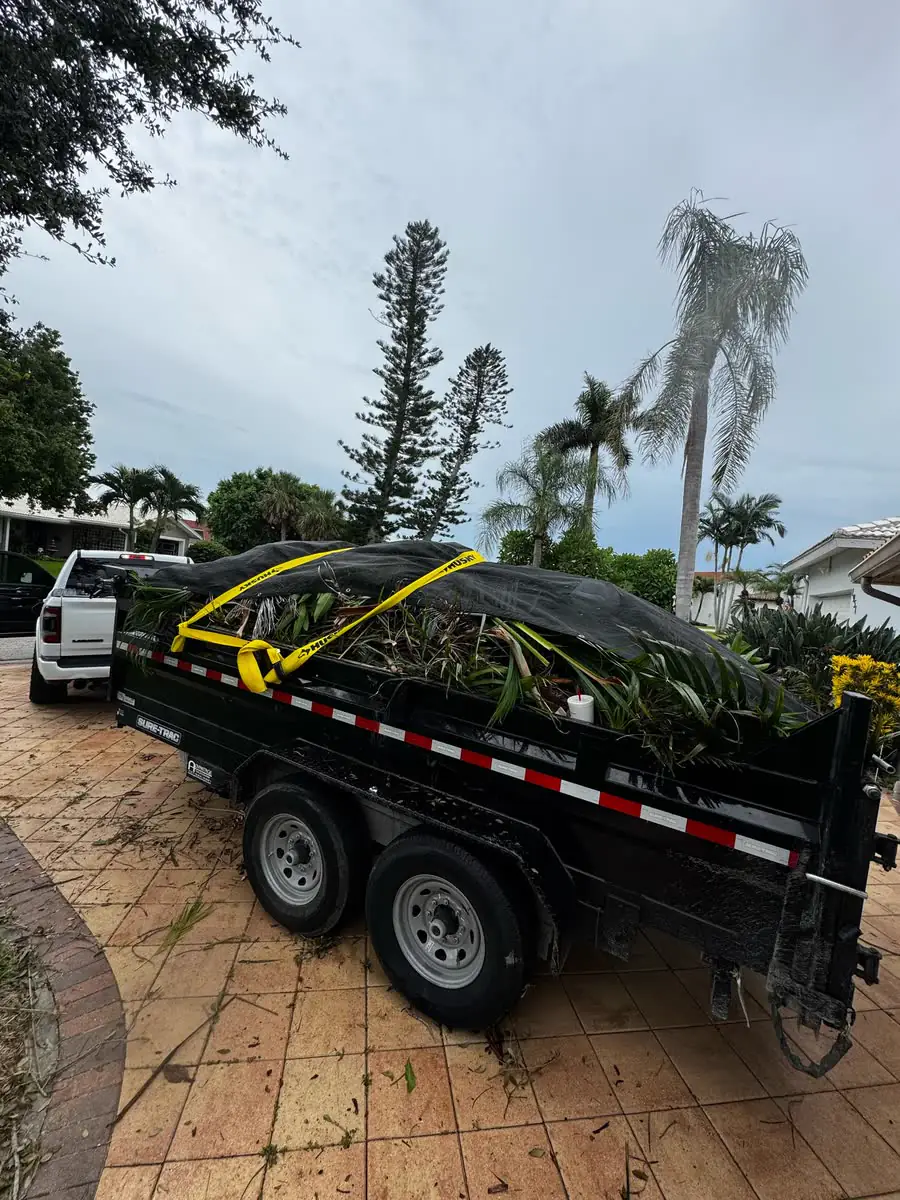 A dump trailer loaded with yard waste on a paver driveway.