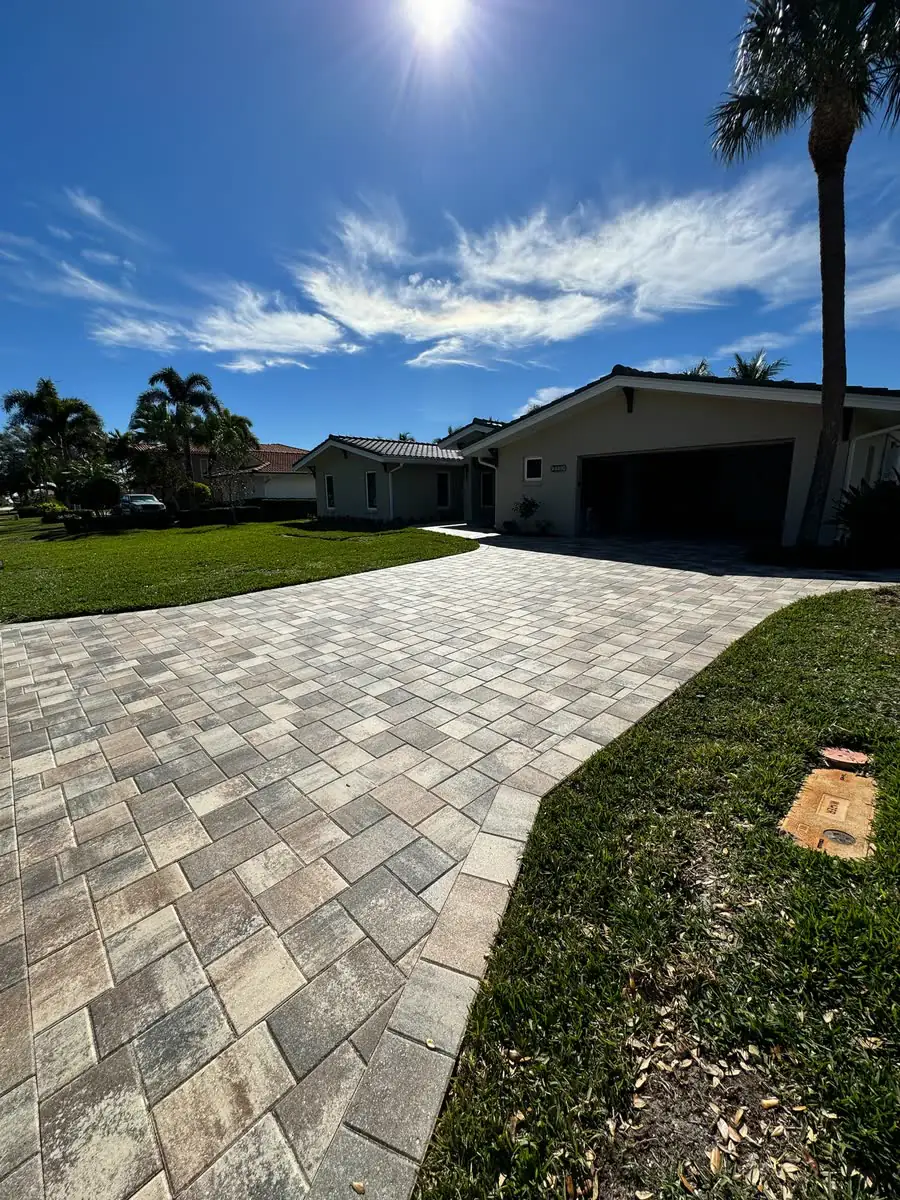 A grey paver driveway between lawns under a bright sun.
