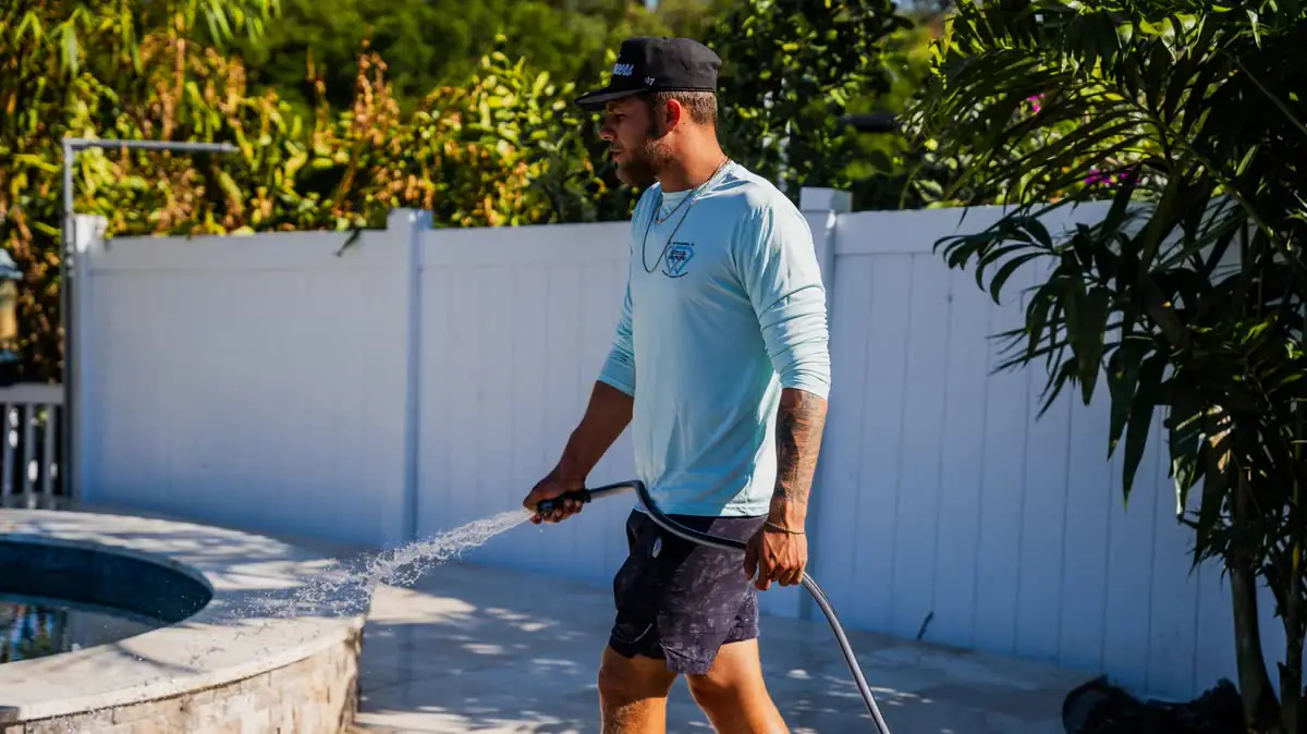 One of the crew washing along a white fence with a wand.