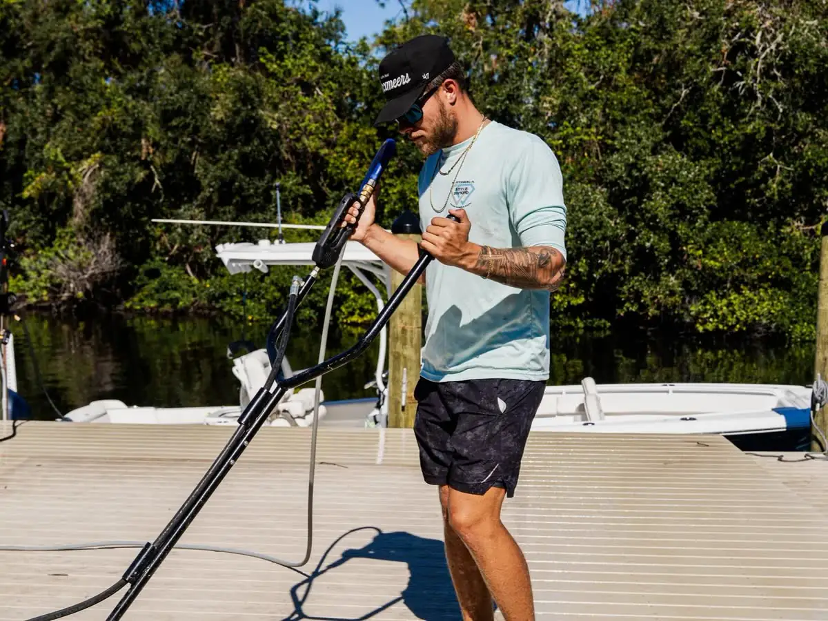 One of the crew washing a deck by the water with a long wand.