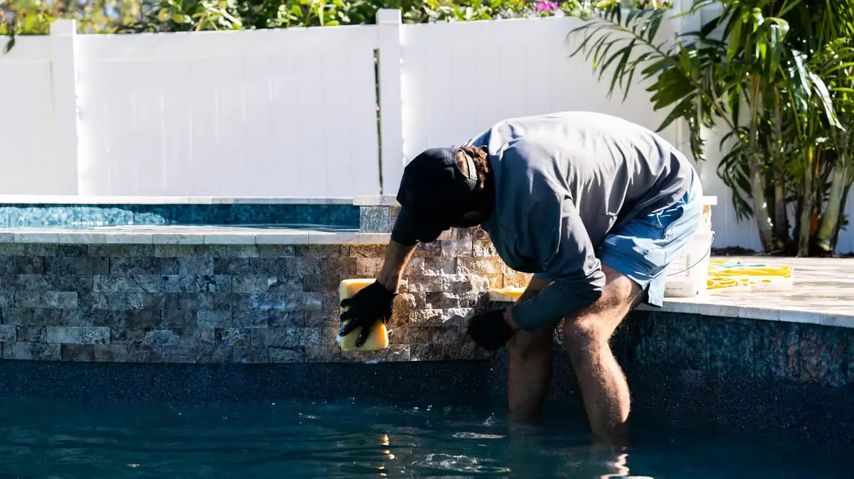 One of the crew cleaning the tile line of a pool.