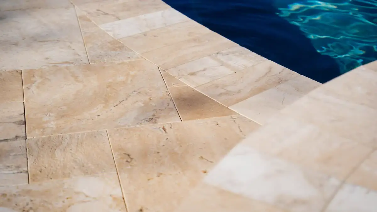 Tan travertine coping at a pool edge, close up.