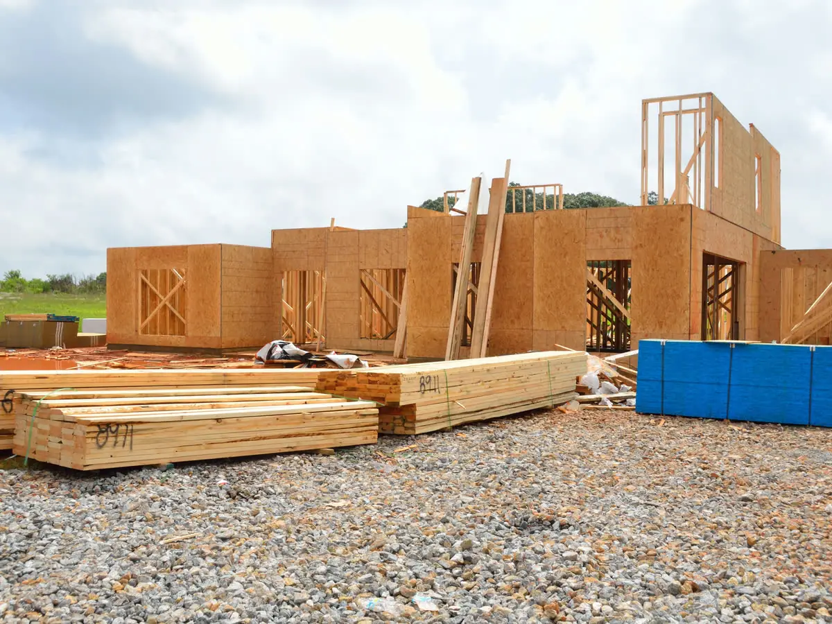 Lumber stacked on a lot beside a house frame going up.