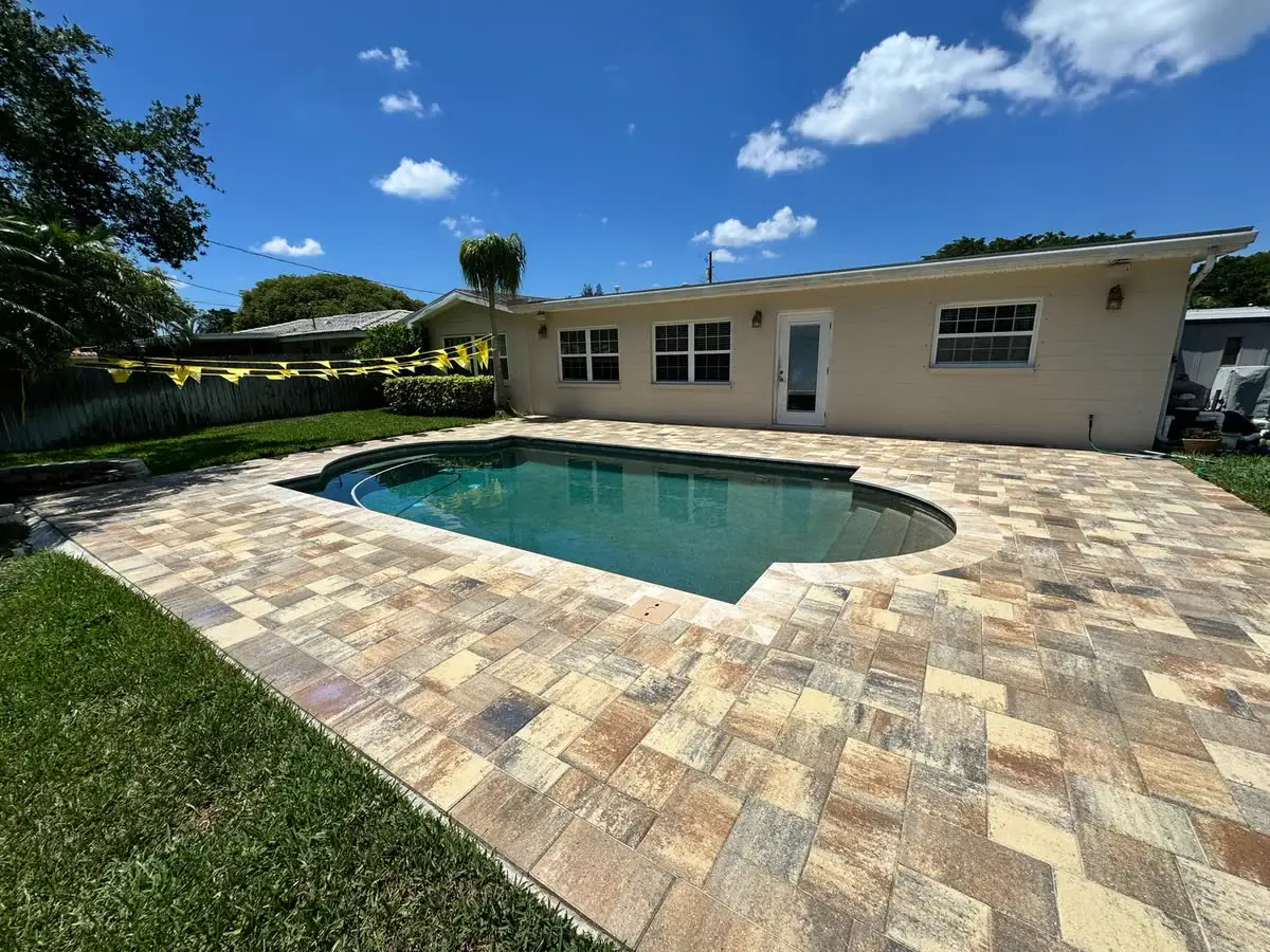 A paver pool deck behind a cream house, the pavers clean and even.