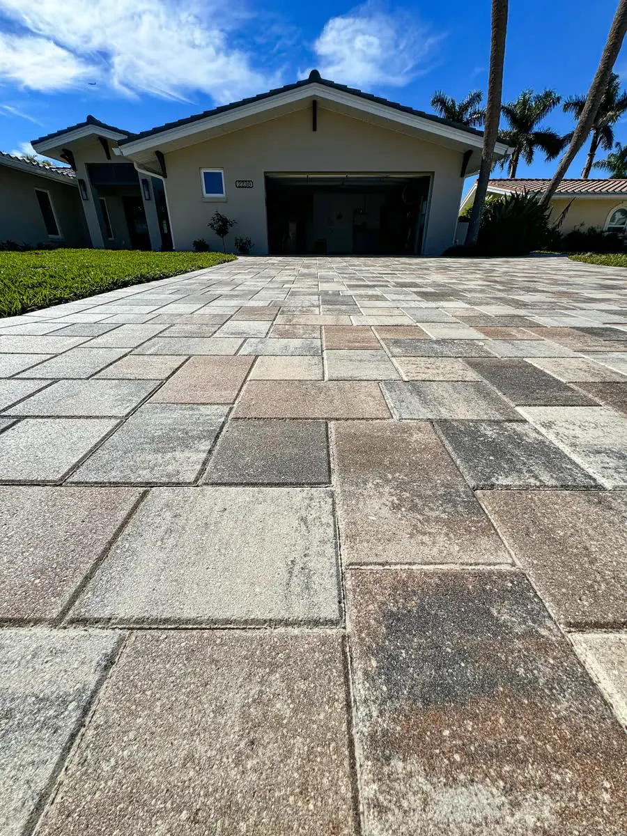 A driveway of large grey and tan pavers in front of a house.