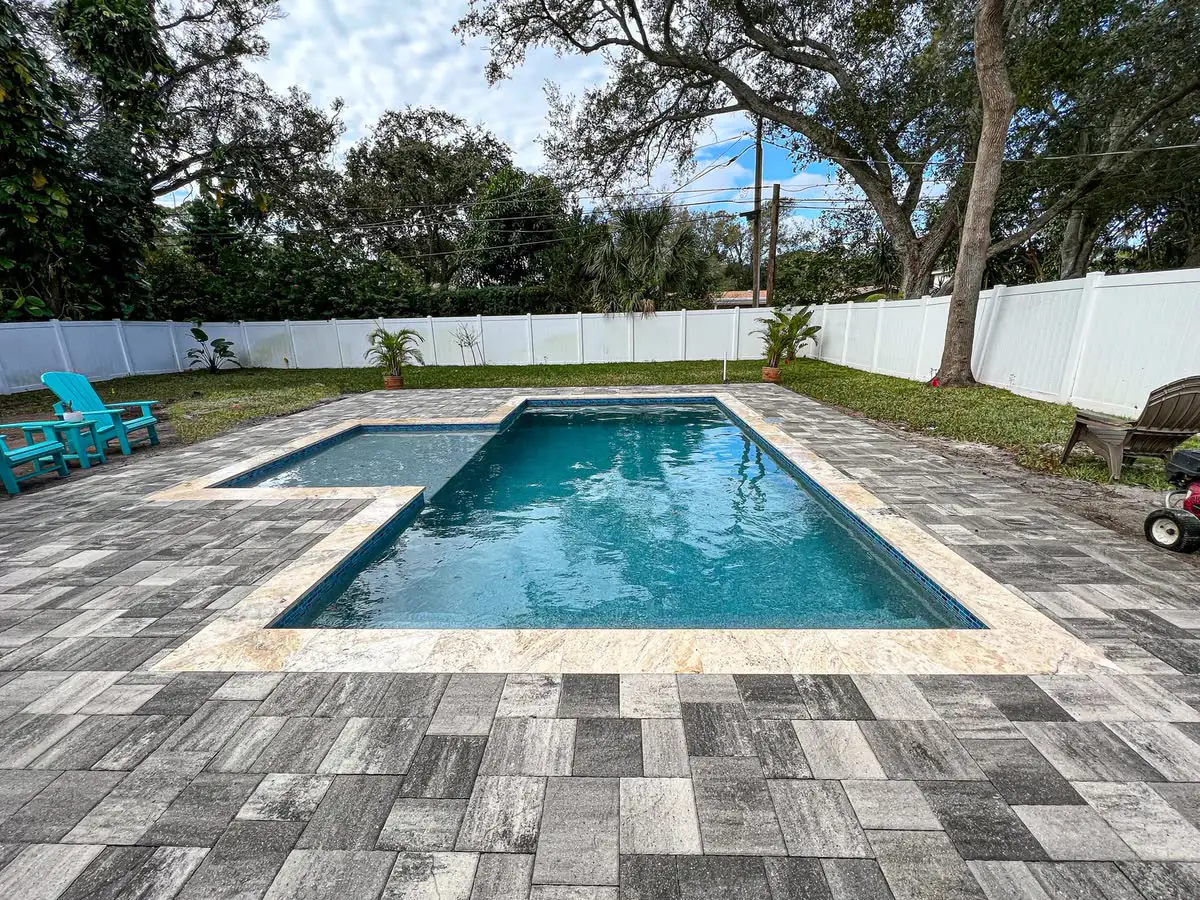 A grey paver deck around a rectangular pool, big oaks beyond.