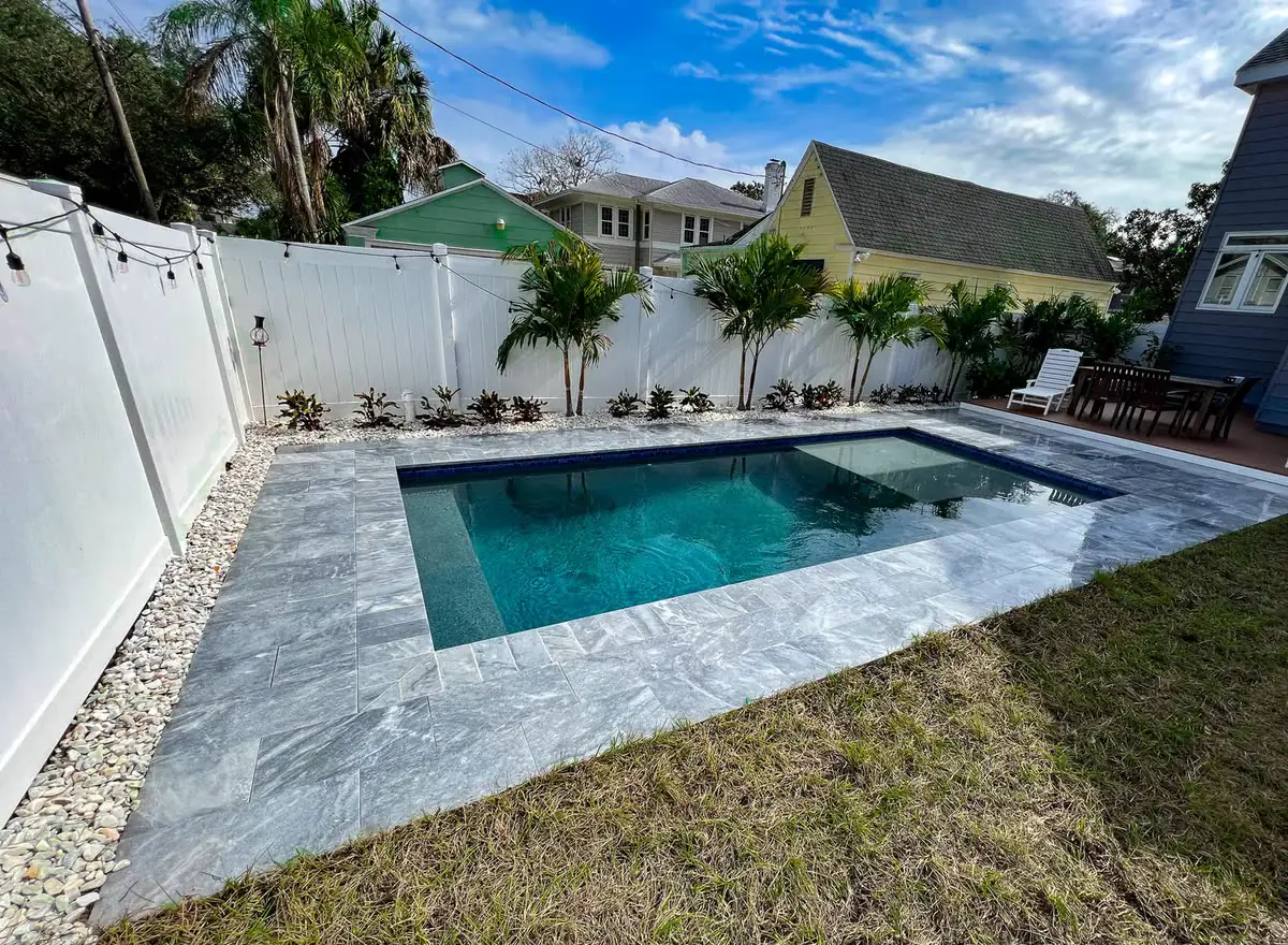 A grey paver pool deck along a white fence.