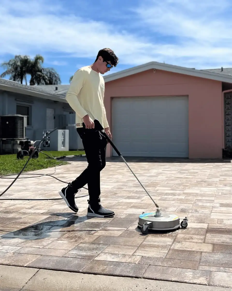 One of the crew running a surface cleaner on pavers in front of a garage.