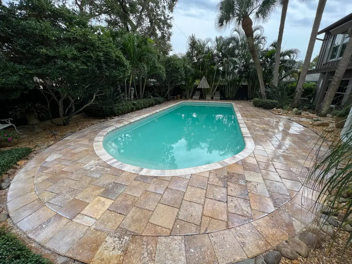 A kidney-shaped pool with a travertine deck, seen from above.