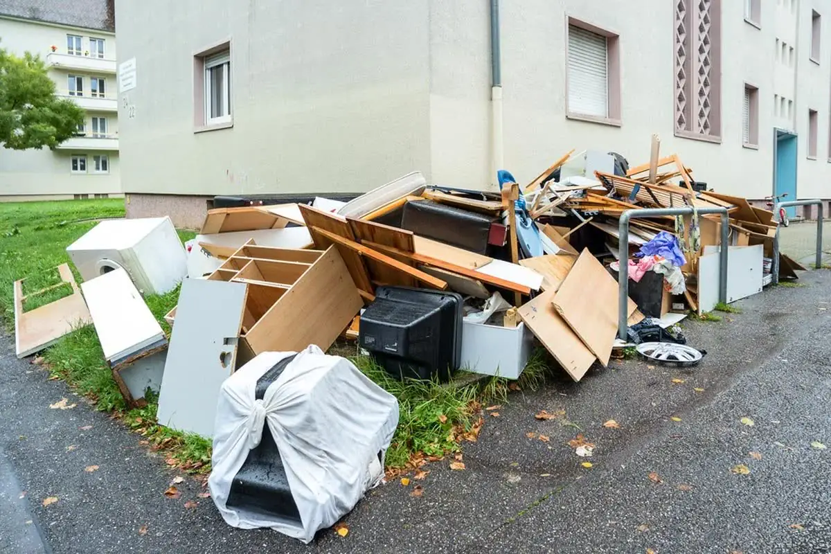 Old furniture and boxes piled up for junk removal beside a building.