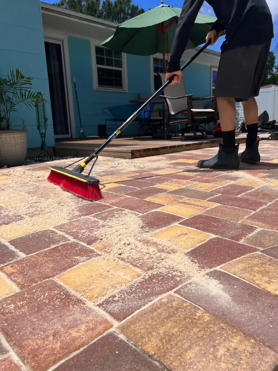 Sweeping joint sand across red, tan and yellow brick pavers with a red push broom.