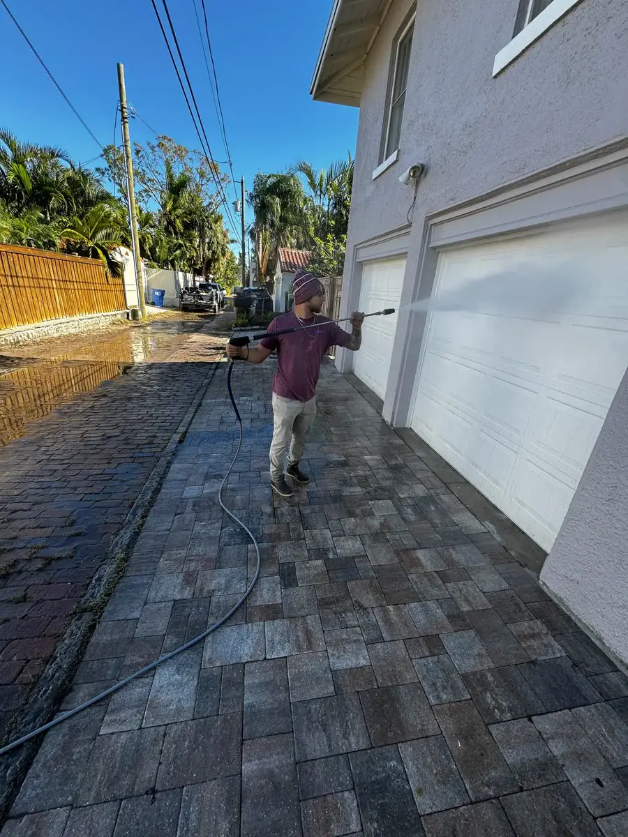 Washing a paver driveway beside a white house.
