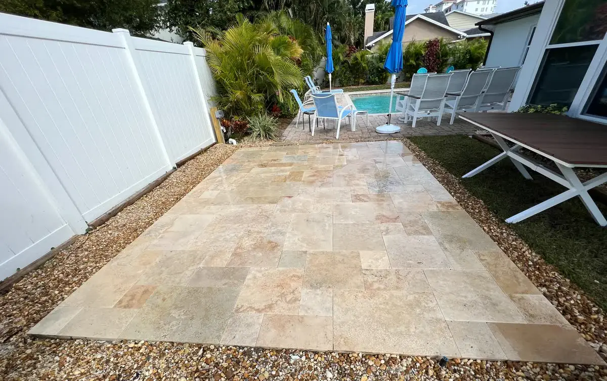 A travertine walk along a white fence to a pool deck.