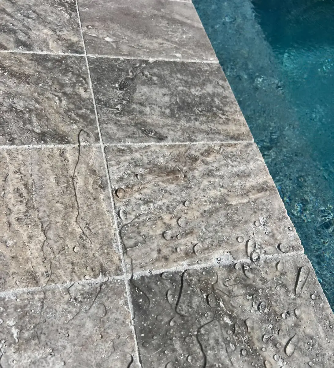 Grey travertine at the edge of a pool, close up.