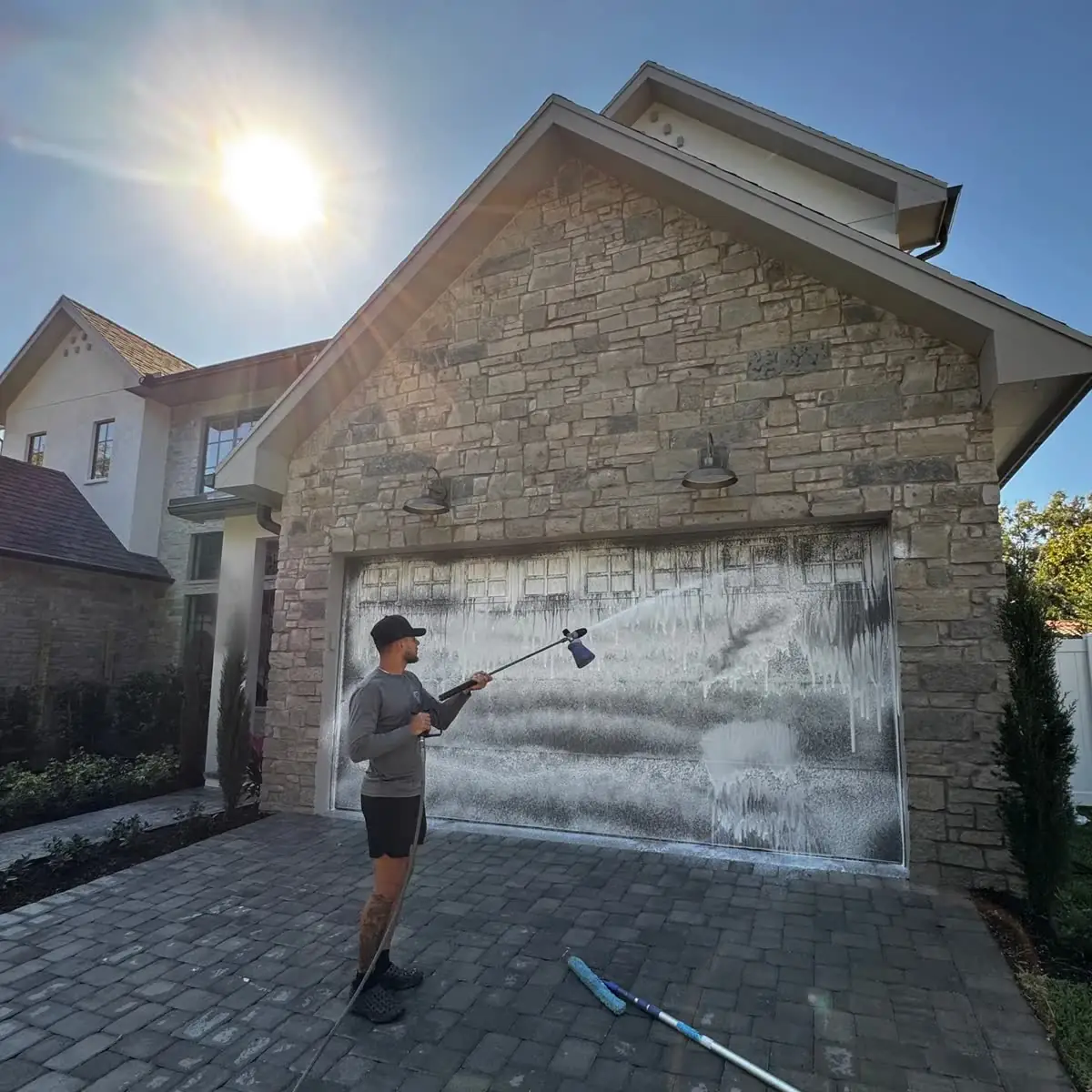 One of the crew soft washing a garage door on a stone house, the foam running down it.