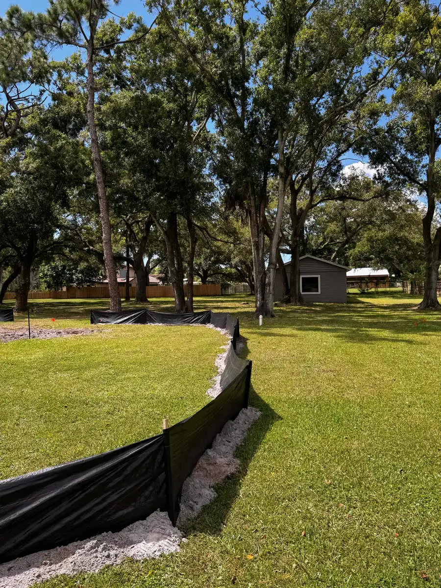 A black silt fence along a lawn under oaks.