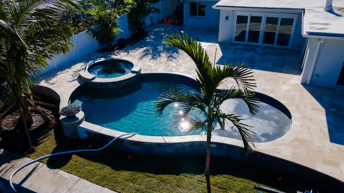 From above: a pool and spa with a travertine deck and palms.