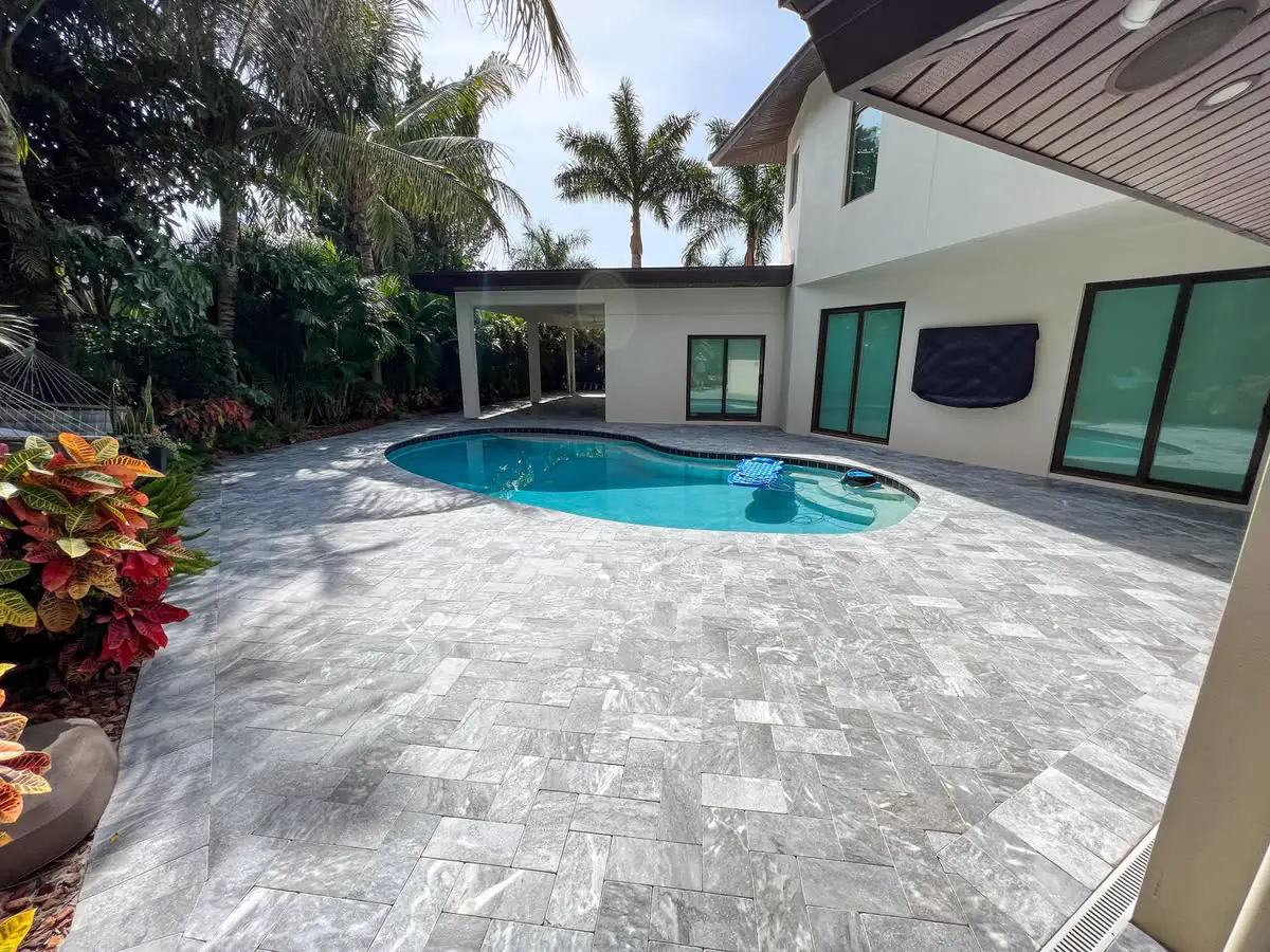 A pale stone pool deck beside a modern house.