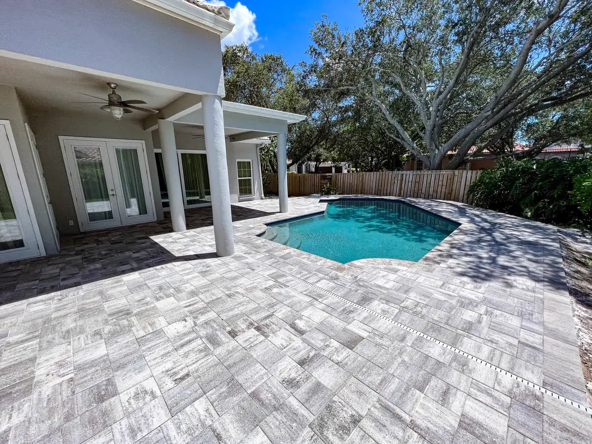 A grey paver patio around a small pool behind a white house.