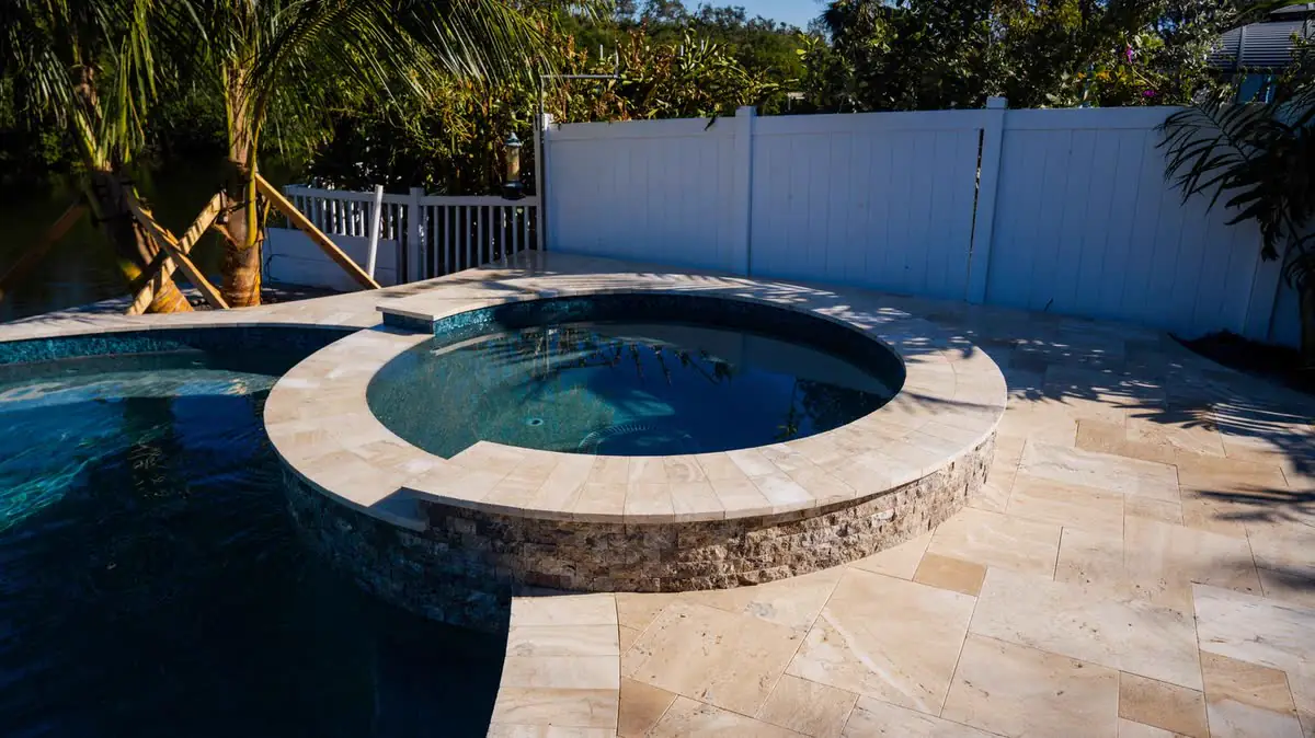 A round spa raised above a pool, travertine deck around it.