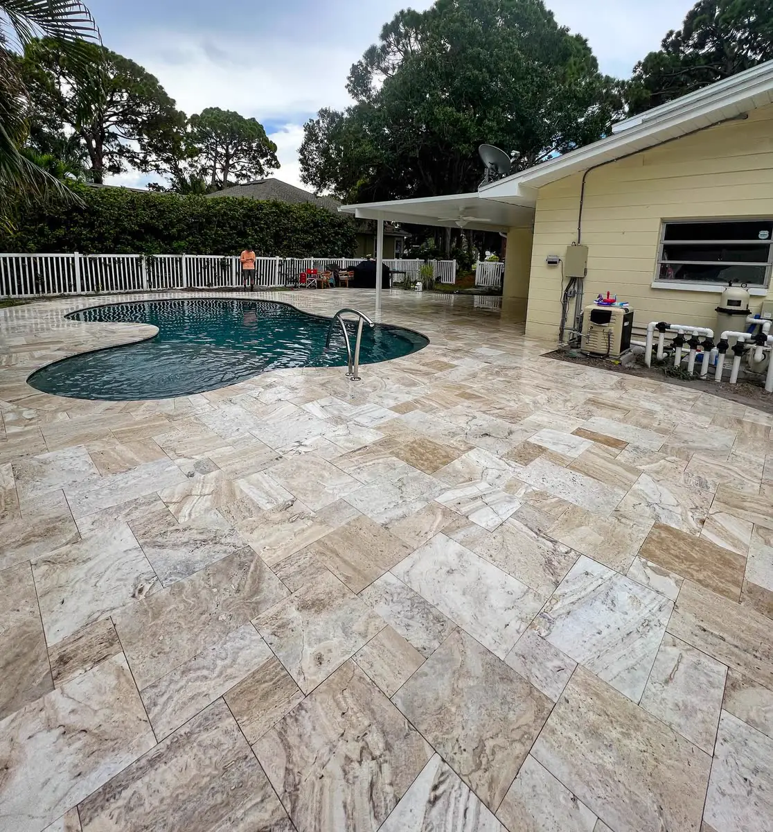 A travertine pool deck around a kidney-shaped pool.