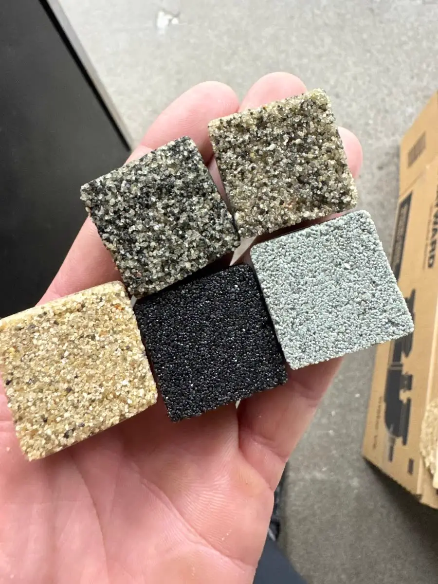 A hand holding four color samples of permeable joint sand.
