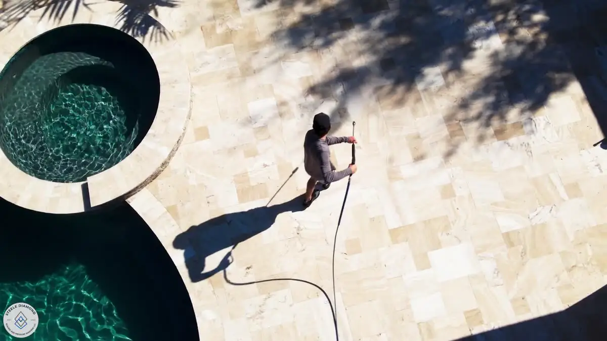 From above: one of the crew washing a travertine deck beside a round spa.