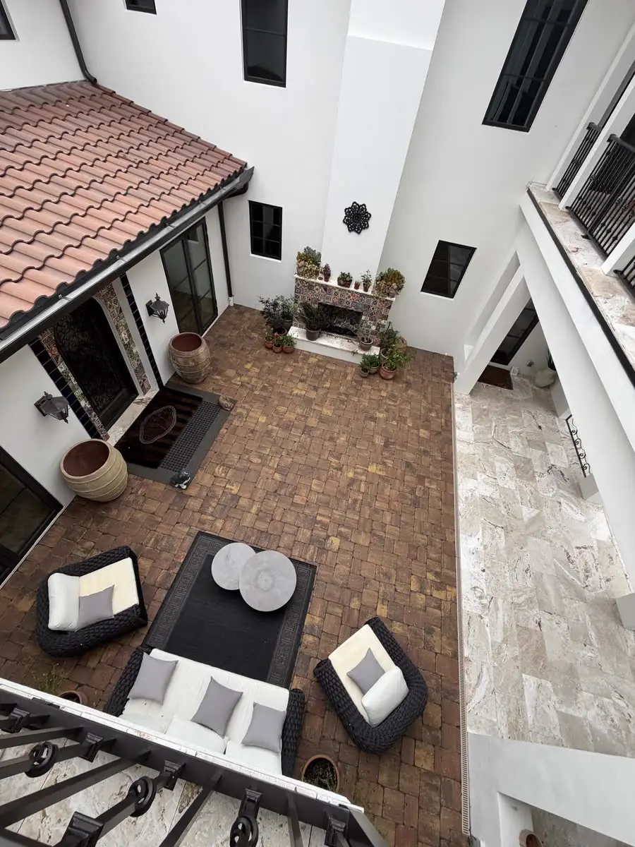 A brick paver courtyard seen from a balcony, with outdoor sofas and potted plants.