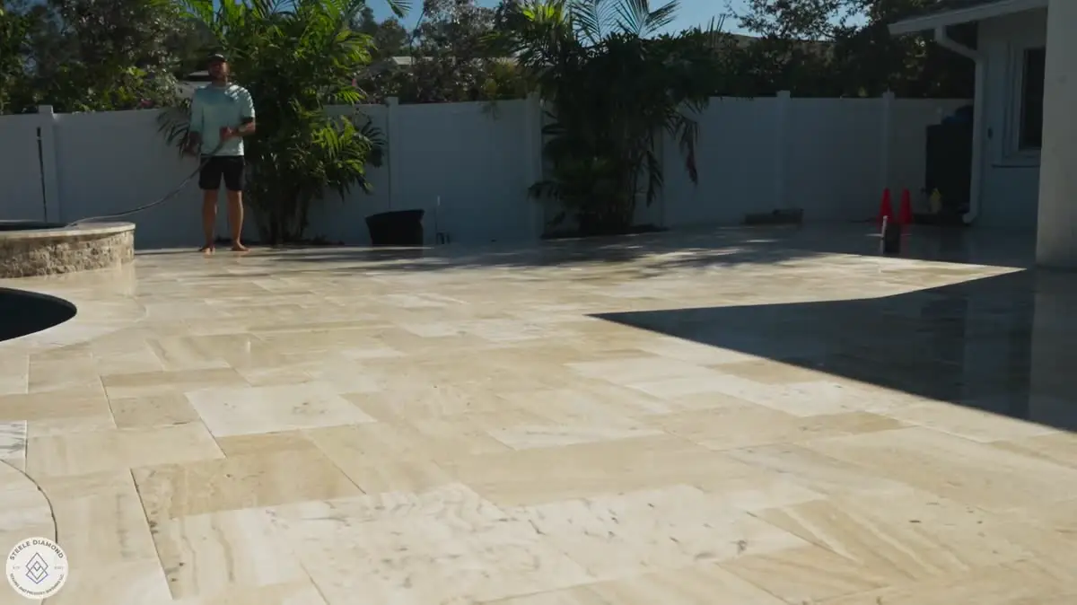 A wide travertine pool deck along a white fence, finished.