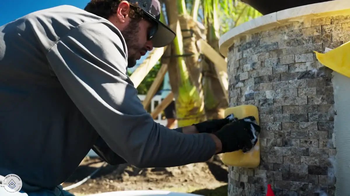 One of the crew working a sponge over a stacked-stone column by a pool.