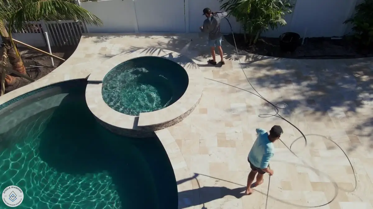 From above: the crew pressure washing a travertine pool deck beside a pool and spa.