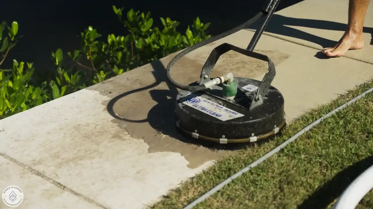 A surface cleaner on a concrete walk beside the grass.