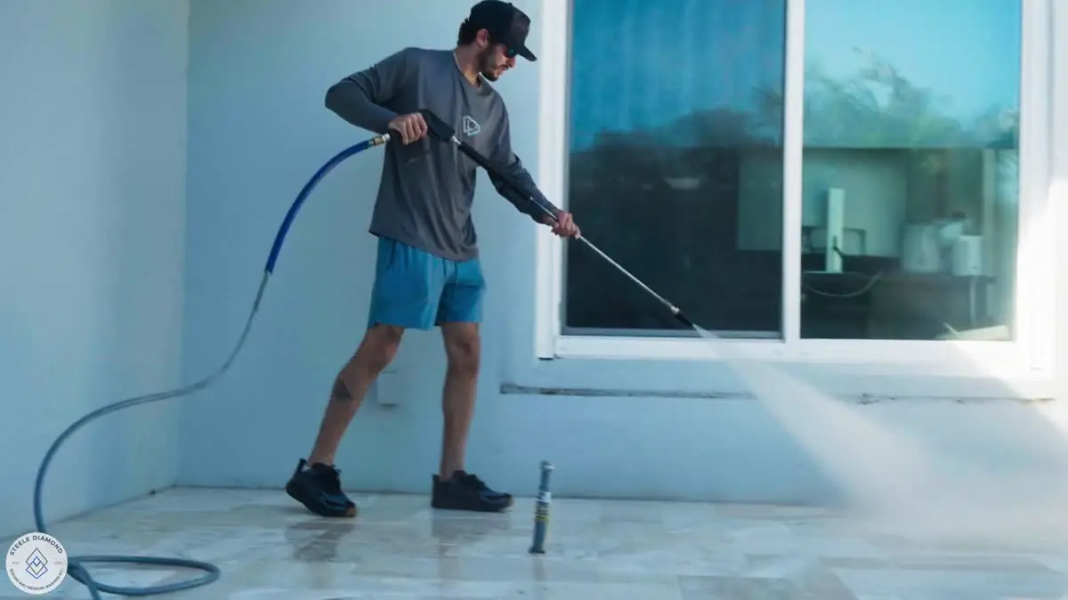 One of the crew pressure washing a pool deck beside sliding glass doors.