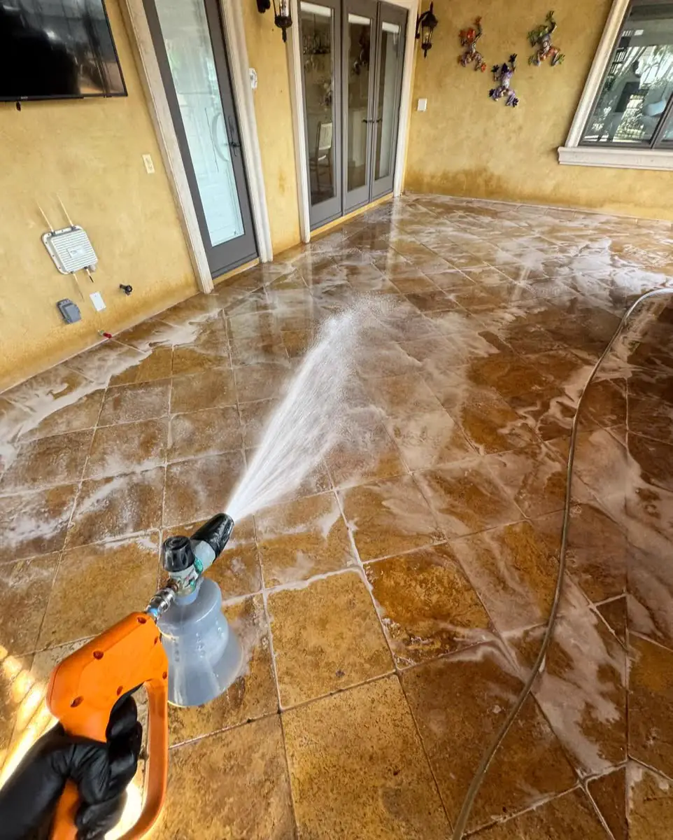 Pressure washing a stone patio under a covered lanai, the wet tile shining.